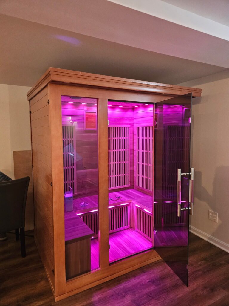 Wooden infrared sauna with pink interior lighting.