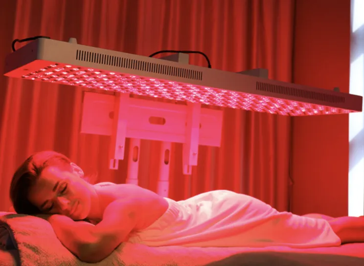 Woman relaxing under red light therapy device.